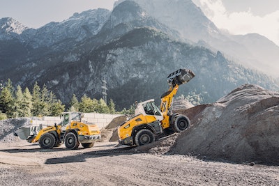 two Liebherr L526 wheel loader by dirt pile mountains background