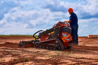 Ditch Witch SK1750 stand-on mini skid steer operator in hard hat on red clay grading