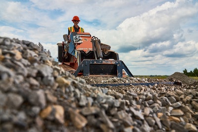 Ditch Witch SK1750 stand-on mini skid steer riding over broken rocks