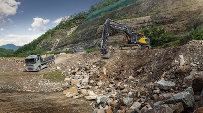 Volvo EC500 Excavator digging in rock quarry with haul truck