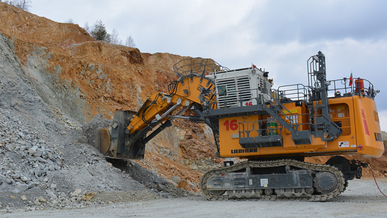 Large orange Liebherr excavator with an extended bucket loading rock rubble at a quarry site on a gravel ground.