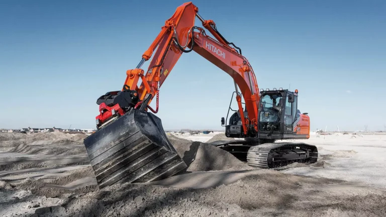 Orange Hitachi excavator scooping dirt at a construction site on a clear day, with a wide bucket digging into the ground.