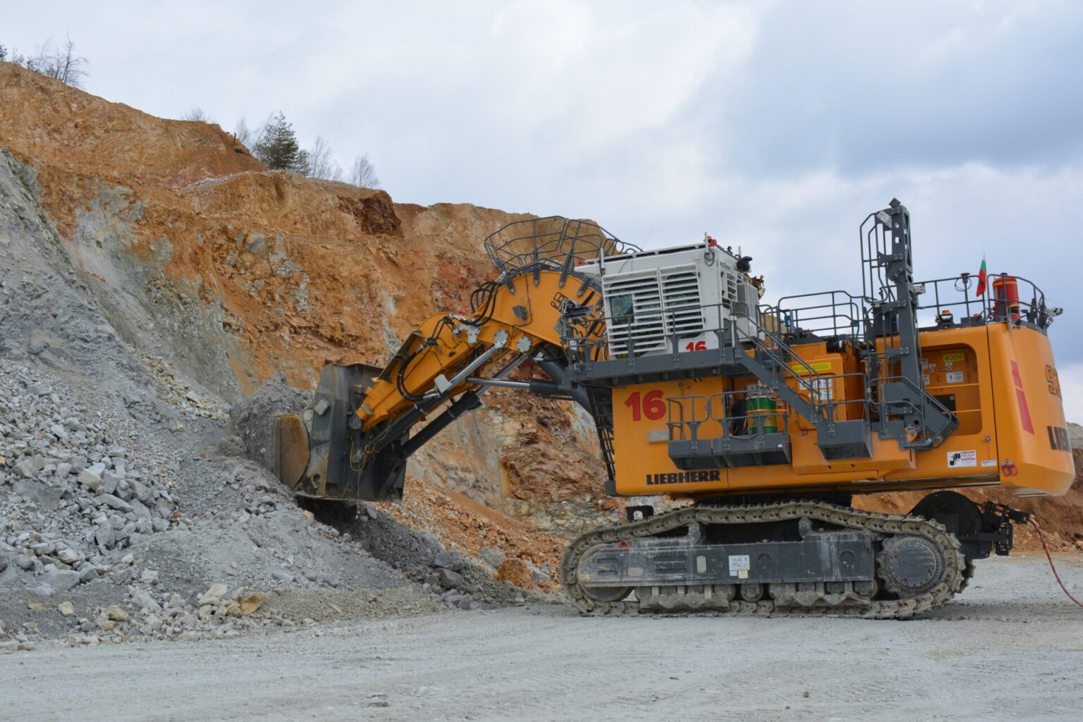 Large yellow Liebherr excavator at a quarry, digging beside a rocky orange cliff.