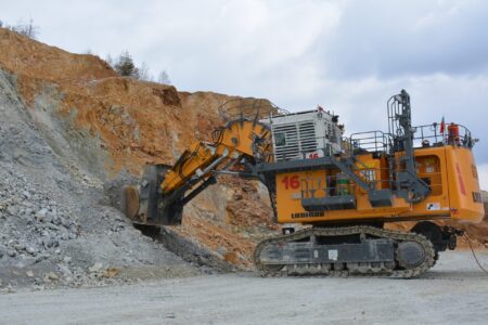 Large yellow Liebherr excavator at a quarry, digging beside a rocky orange cliff.