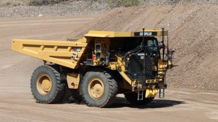 Large yellow Caterpillar mining dump truck driving on a dusty quarry road.