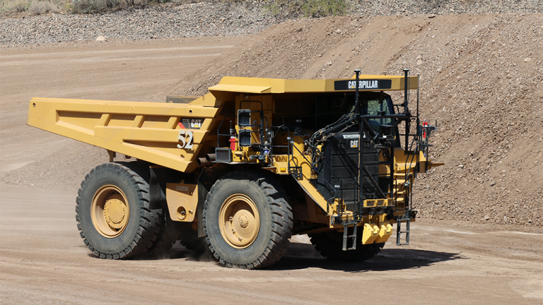 Large yellow Caterpillar mining dump truck driving on a dusty quarry road.