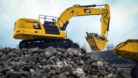 Yellow CAT excavator on a rocky pile, lifting a bucket loaded with rocks at a construction site