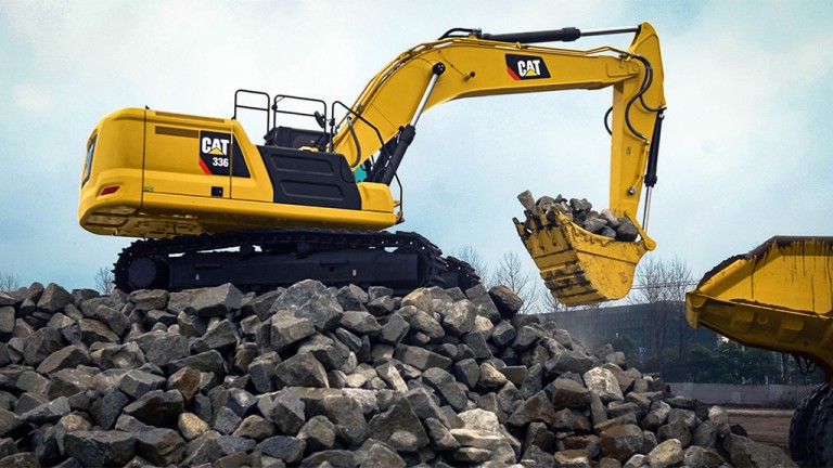 Yellow CAT excavator on a rocky pile, lifting a bucket loaded with rocks at a construction site