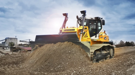 Yellow Liebherr bulldozer pushing a dirt pile at a construction site.