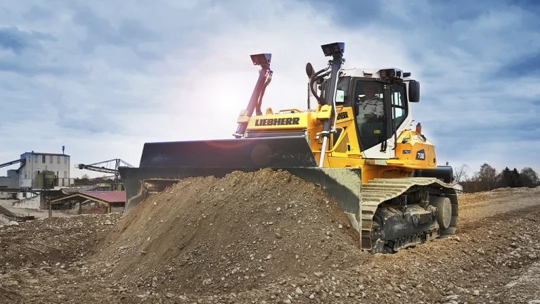 Yellow Liebherr bulldozer pushing a dirt pile at a construction site.