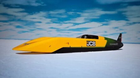 Yellow and black jet-powered land speed car on a salt flat with a JCB logo, blue sky, streamlined cockpit and long pointed nose.
