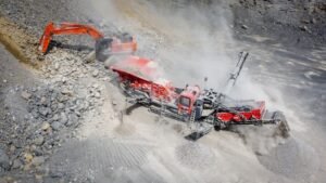 Red rock crushing plant operating in a dusty quarry, breaking and sizing gravel.