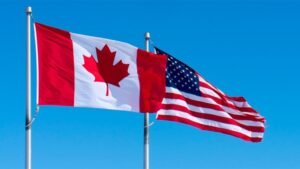 1779389615_63596_en_c9ac5_65713_canada-us-flagjpg - Machines Wiki Canada and United States flags waving side by side on flagpoles against a bright blue sky, symbolizing the two nations.