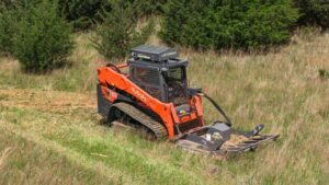 1779493483_63695_en_c379d_65826_loftness-kwik-cut-brush-cutterjpg - Machines Wiki Orange Kubota compact track loader with a front-mounted mower attachment cutting grass on a hillside field in woodland edge landscape.