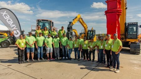 1779749503_63649_en_818bd_65775_groupe-gymdex-teamjpg - Machines Wiki Group of about 20 workers in lime shirts posing in front of heavy machinery at an outdoor construction expo.