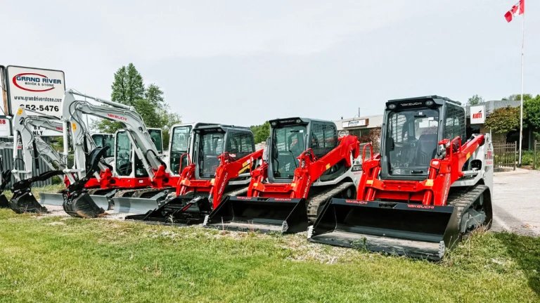 1779849222_63713_en_f0e87_65844_cornerstone-equipment-takeuchipng - Machines Wiki Lineup of red-and-black mini excavators with large front buckets parked on a gravel lot beside a grassy area at a dealership.