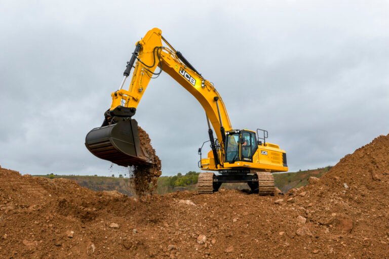 520x-tracked-excavators-stage-v-application-imagejpg - Machines Wiki Yellow JCB excavator in a construction site scooping dirt with its bucket against a mound under a cloudy sky.