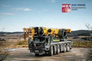 Large mobile crane truck with a yellow crane extended on a concrete area, rural landscape behind; SERA 2026 Environmental Award logo in the top-right corner.