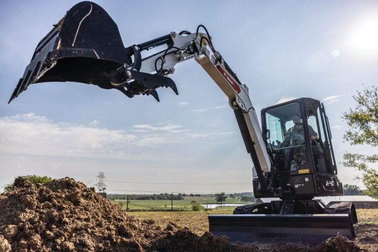 905x0_s3-71325-MNSW-EX-CYCLE-TIMES-1jpg - Machines Wiki Excavator with digging bucket raised over a dirt pile at a construction site under a bright blue sky