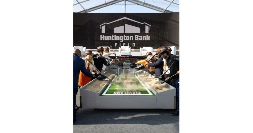 905x0_s3-71339-M-OH-BROWNS-LAUNCH-1jpg - Machines Wiki Diverse group in hard hats surrounding a sandbox football field at Huntington Bank Field groundbreaking event.