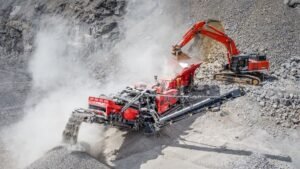 Red rock-crushing and conveying machine at a dusty quarry slope in operation.