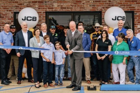 Business ribbon-cutting ceremony outside a brick storefront with JCB balloons and a crowd of community members.