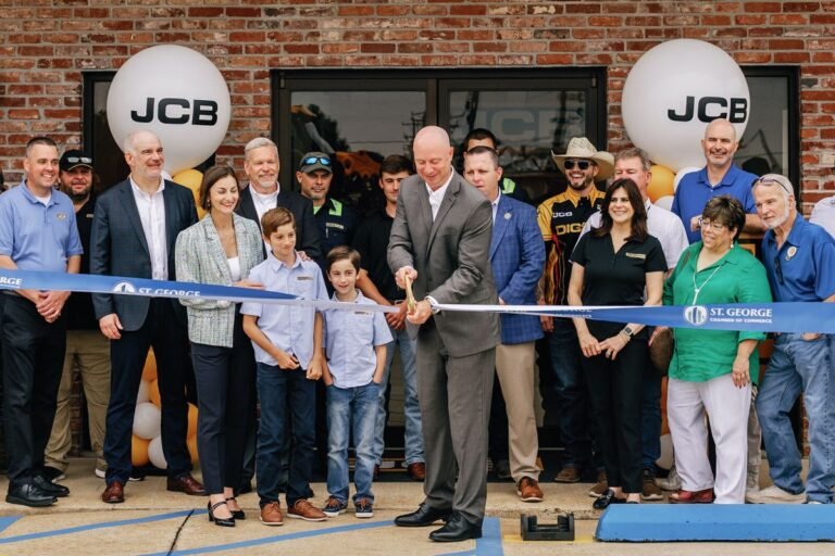 905x0_s3-71381-SW-GCJCB-OPEN-1_jpegjpg - Machines Wiki Business ribbon-cutting ceremony outside a brick storefront with JCB balloons and a crowd of community members.
