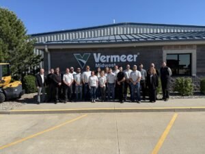 905x0_s3-71396-Charleston_jpegjpg - Machines Wiki A group of Vermeer Midwest employees posing together outside a brick building with the Vermeer Midwest sign and logo visible on the wall.