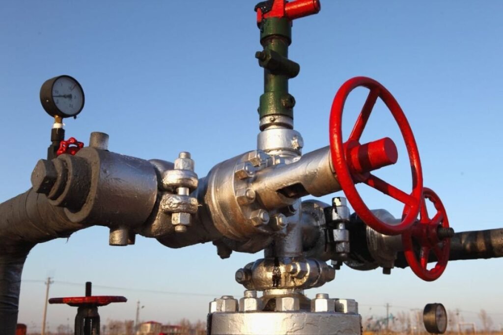Valve assembly with red handwheel and pressure gauge, outdoors, controlling fluid flow.