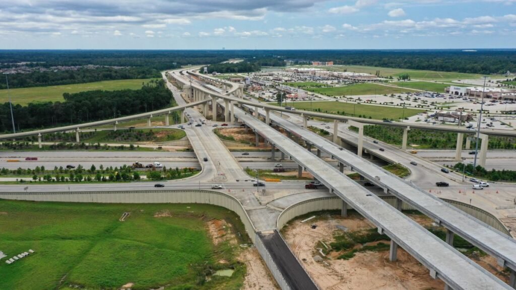 Aerial view of a complex multi-level highway interchange with several overpasses and surrounding commercial area nearby.