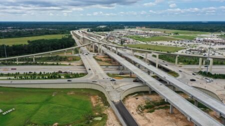 Aerial view of a complex multi-level highway interchange with several overpasses and surrounding commercial area nearby.