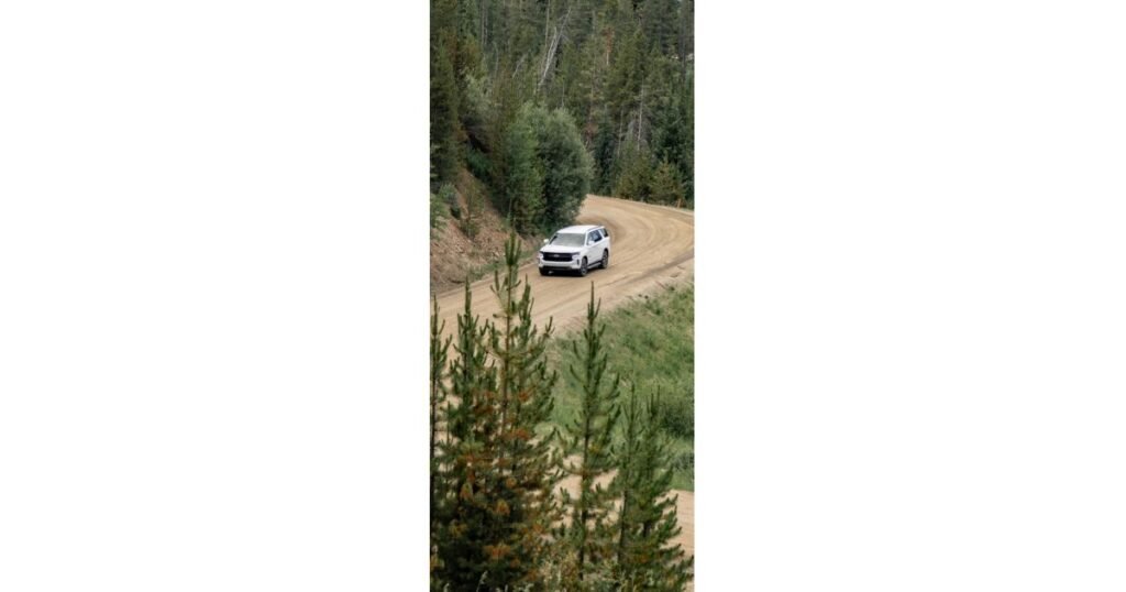 905x0_s3-71441-NE-TRK-PTR-NE-BIZ-1jpg - Machines Wiki Silver SUV driving on a winding dirt road through a pine forest