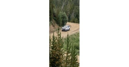 905x0_s3-71441-NE-TRK-PTR-NE-BIZ-1jpg - Machines Wiki Silver SUV driving on a winding dirt road through a pine forest