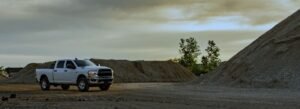White pickup truck parked near large piles of gravel at a quarry or gravel pit