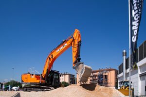 Orange excavator lifting a bucket of dirt at a construction site under a clear blue sky, with DEVELON branding visible on the arm