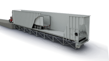 Red semi truck at a loading dock beside a long gray warehouse, with a trailer entering a loading bay under a metal platform.