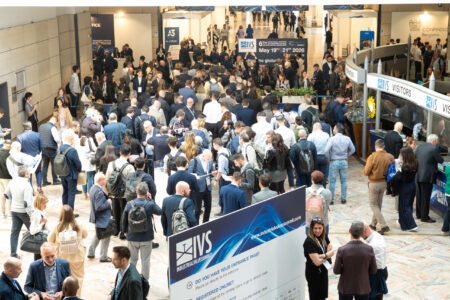 Crowded conference expo hall with attendees, booths, and blue IVS signage overhead.