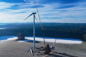 TURBINEjpg - Machines Wiki Wind turbine under construction with a crane beside a snowy field and forest under a blue sky