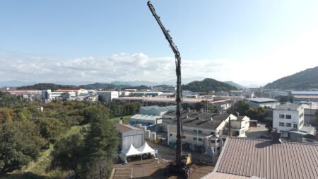 Construction crane dominating a city industrial area under a clear blue sky, with hills in the distance.