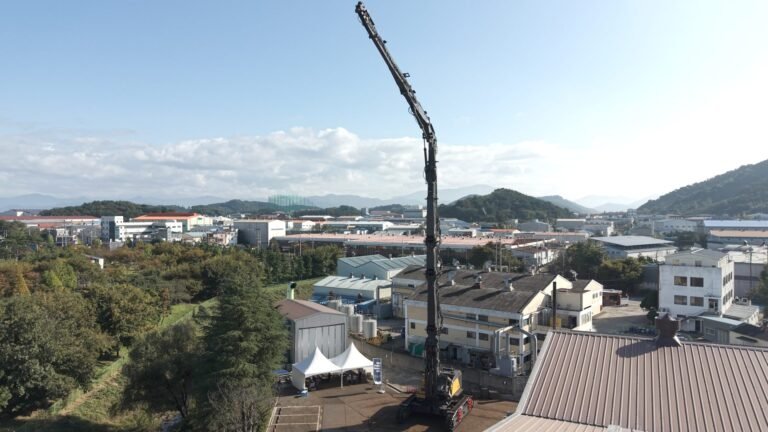 Construction crane dominating a city industrial area under a clear blue sky, with hills in the distance.