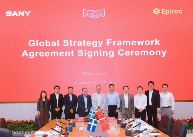 Group of executives posing on a stage in front of an orange backdrop reading 'Global Strategy Framework Agreement Signing Ceremony' with SANY (left) and Epiroc (right) logos; flags and a conference table in the foreground.