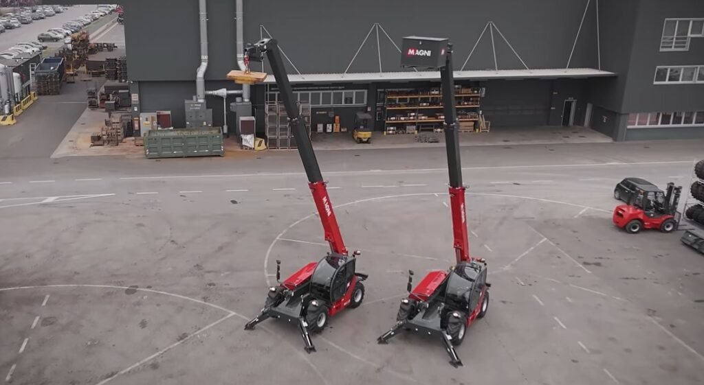 Two red Magni telehandlers with tall black extended booms parked side by side in an industrial yard outside a warehouse site