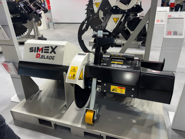 simex-d-bladejpg - Machines Wiki Industrial SIMEX Blade machine on display at a trade show, showing warning stickers, yellow roller and dark metal framework used for cutting or shredding material