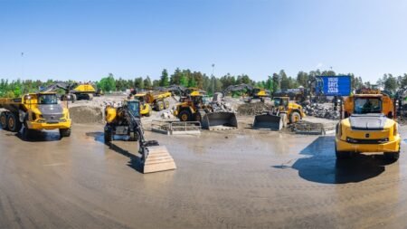 Construction site with multiple yellow heavy machines on a muddy lot and a blue Volvo Days 2016 banner.