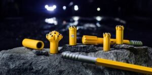 Set of yellow cylindrical rock drill bits and handles arranged on a rough rock surface at night.
