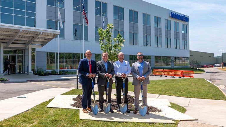 Komatsu opens new mining headquarters Four men in suits with shovels pose for a groundbreaking ceremony outside a modern office building with glass windows and flags nearby.
