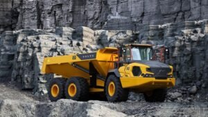 Yellow Volvo A50 articulated dump truck parked on rocky quarry terrain with a dark rock cliff in the background, heavy-duty tires visible.