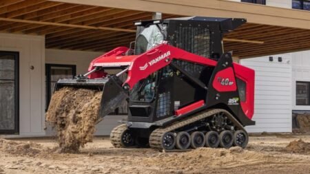 1781544628_63824_en_bd786_65968_yanmar-compact-equipmentjpg - Machines Wiki Red Yanmar compact track loader with a digging bucket dumping soil at a construction site beside a partially built building.