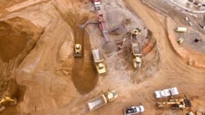 Aerial view of a dirt excavation site with multiple yellow dump trucks and excavators moving soil around large piles.