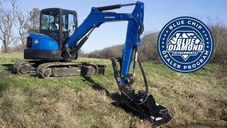 1781740260_63834_en_8e496_65978_blue-diamond-brush-cutter-blue-chip-dealerjpg - Machines Wiki Blue compact excavator with hydraulic arm and bucket on a grassy field, featuring a Blue Diamond Attachments program badge on the right side.